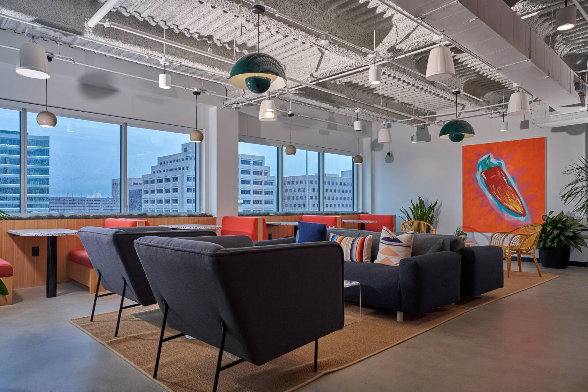 Modern office lounge with couches, art, and large windows overlooking city buildings.