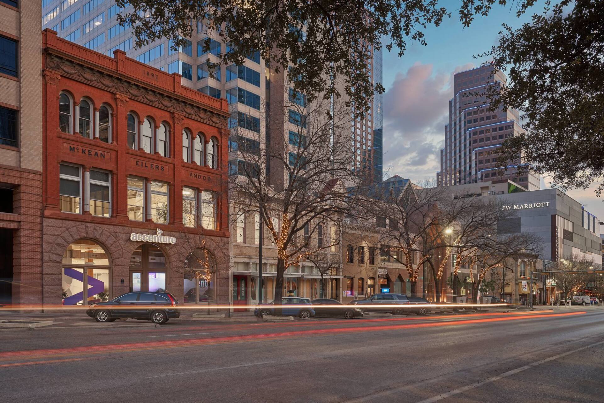 Brick building with archways in a city street, with cars and tall buildings.