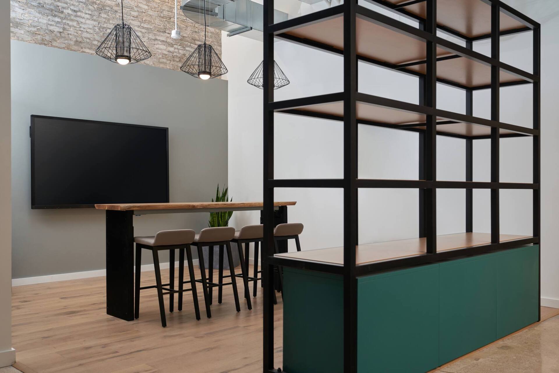 Modern office space with wooden floor, green and black shelving, large TV, bar table, and stools.