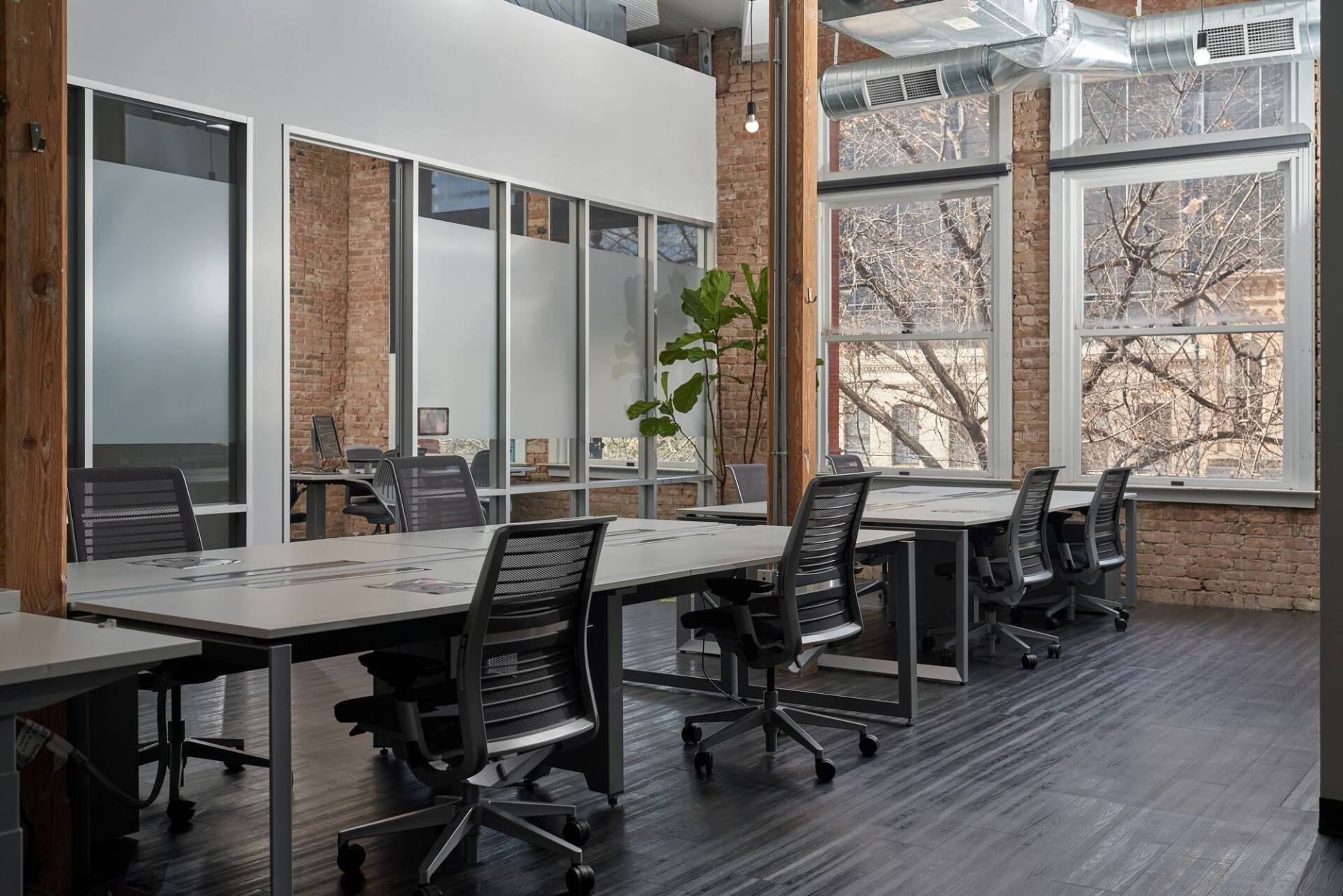 Office space with desks, chairs, exposed brick walls, and large windows.