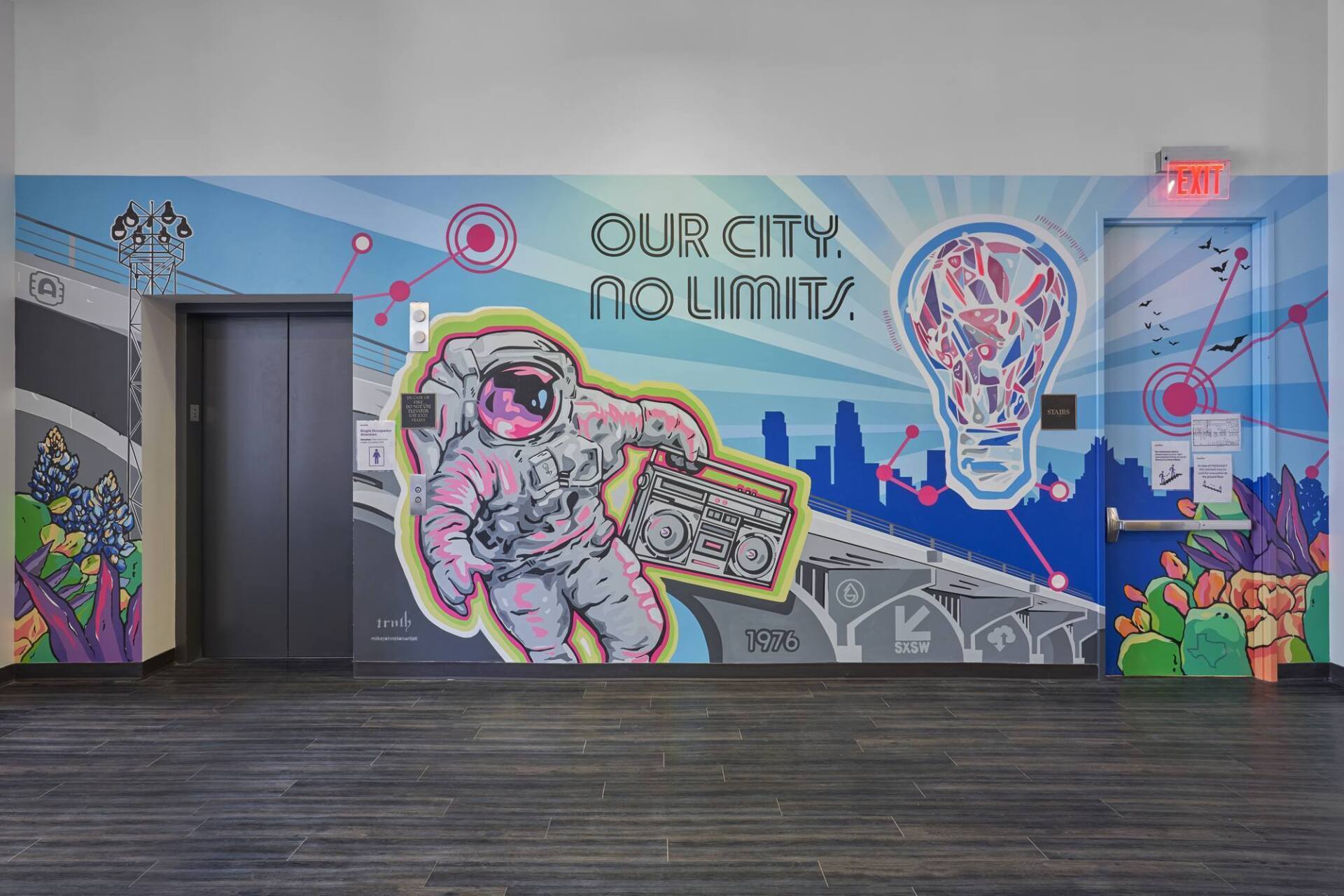 A mural with an astronaut holding a boombox, a cityscape, and a lightbulb on a wall between two elevator doors.