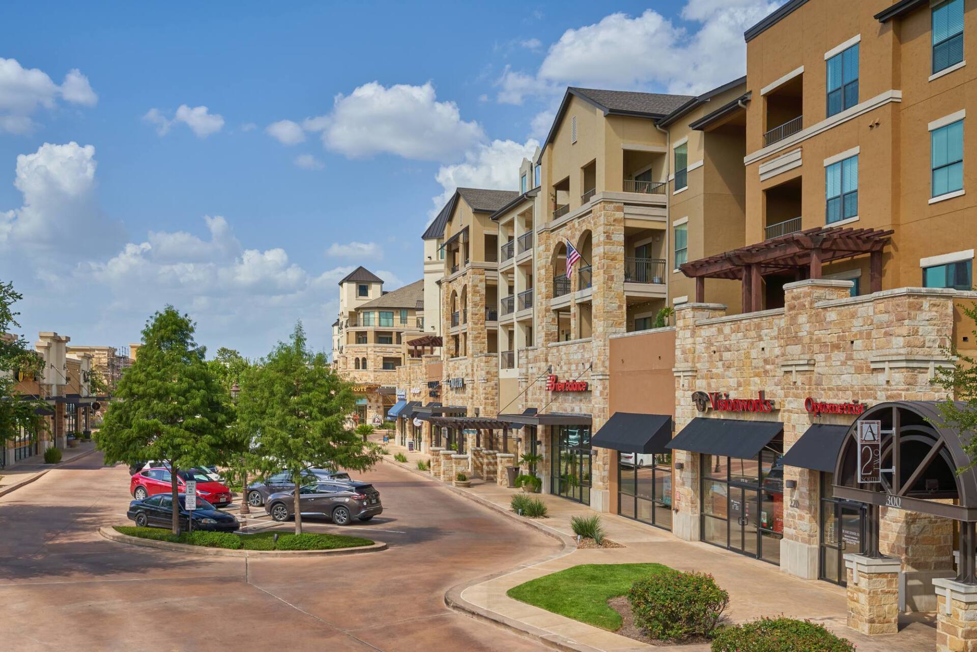 Apartment building with shops on the ground level. Cars parked on the street. Blue sky with clouds.