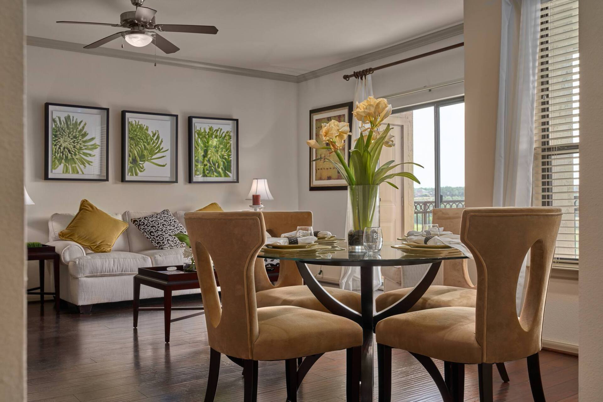 Dining area with glass table, yellow chairs, and sofa. Artwork and flowers.