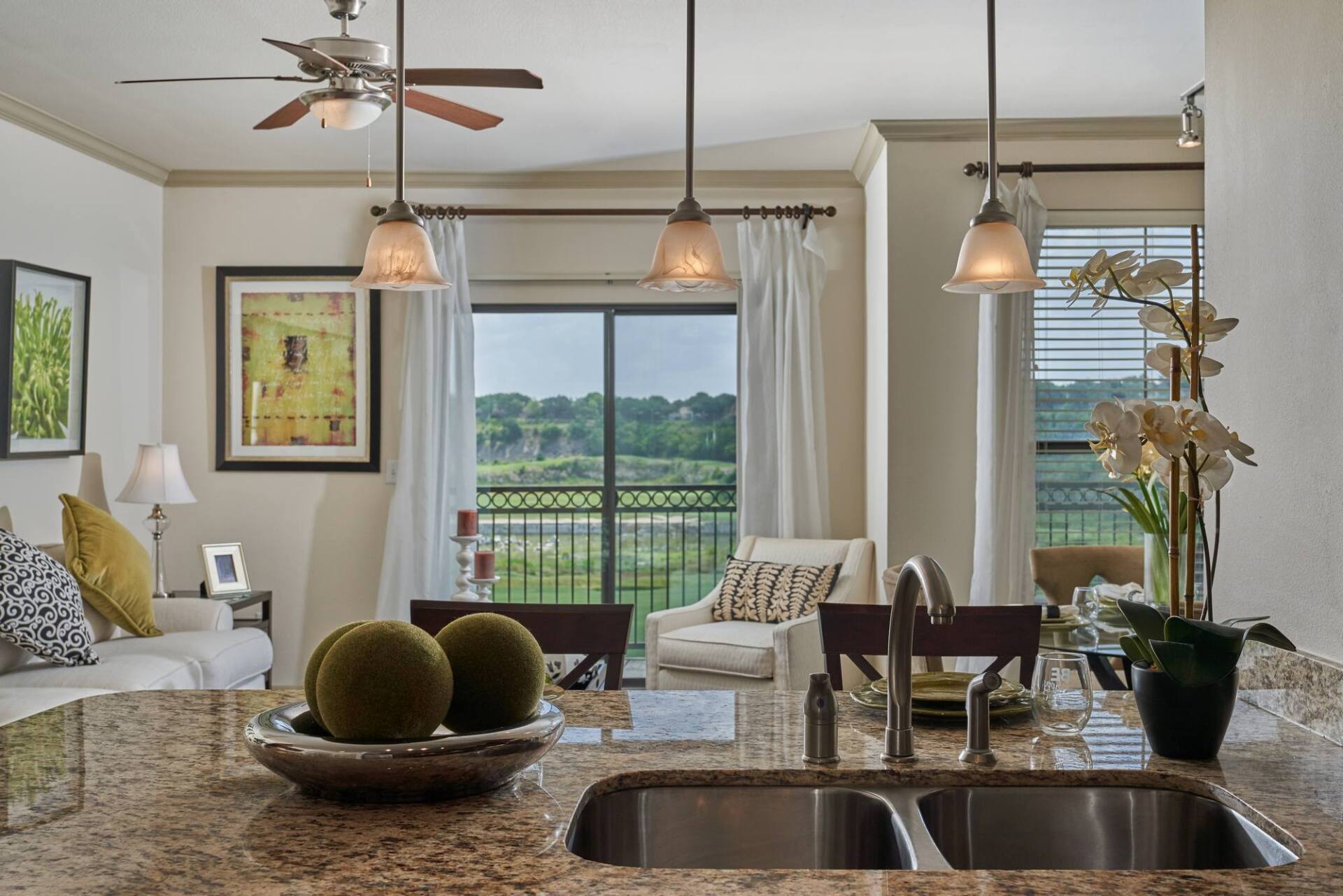 A modern kitchen with a view, featuring a granite countertop, pendant lights, and a balcony.
