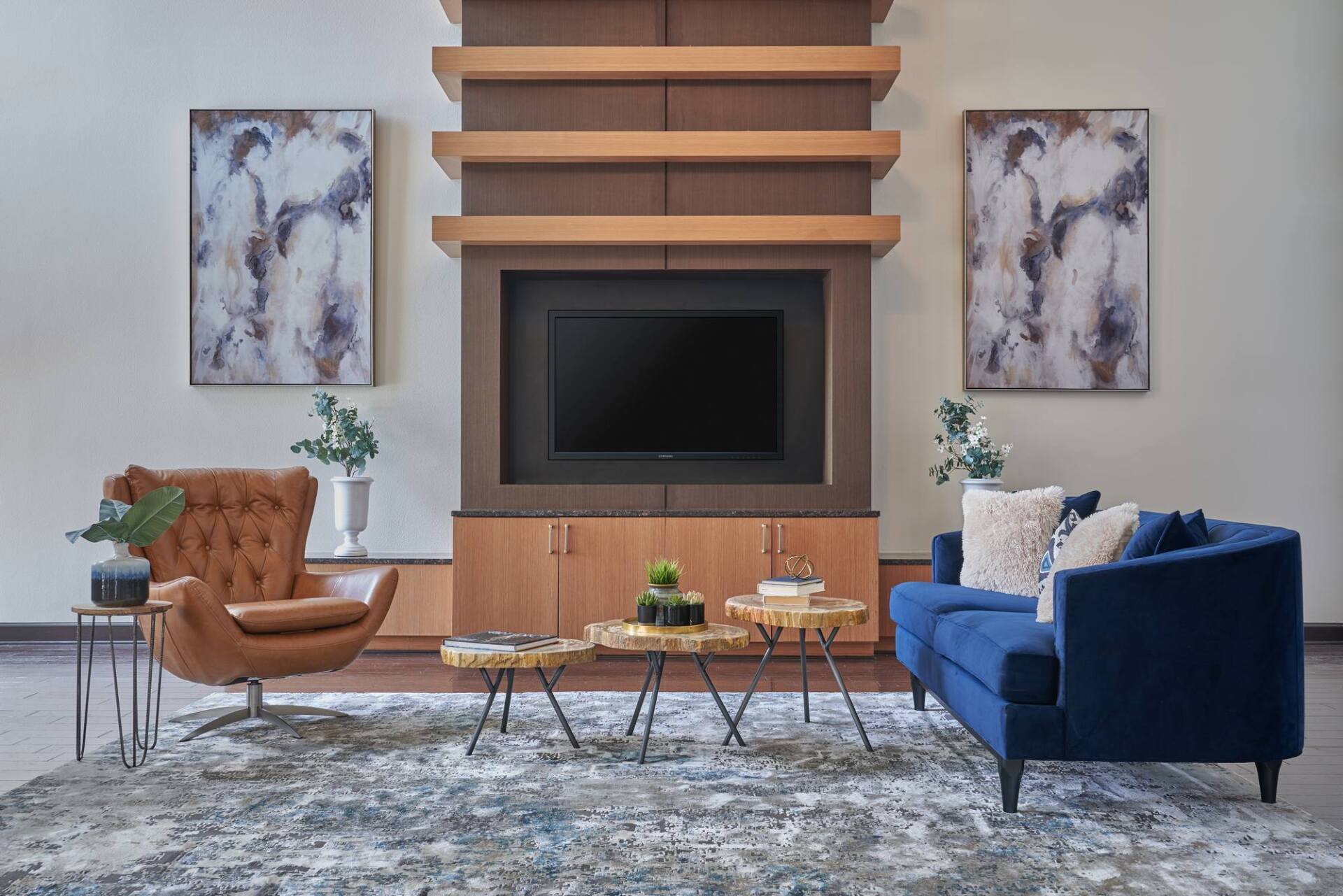 Living room with blue sofa, leather chair, TV, artwork, and patterned rug.