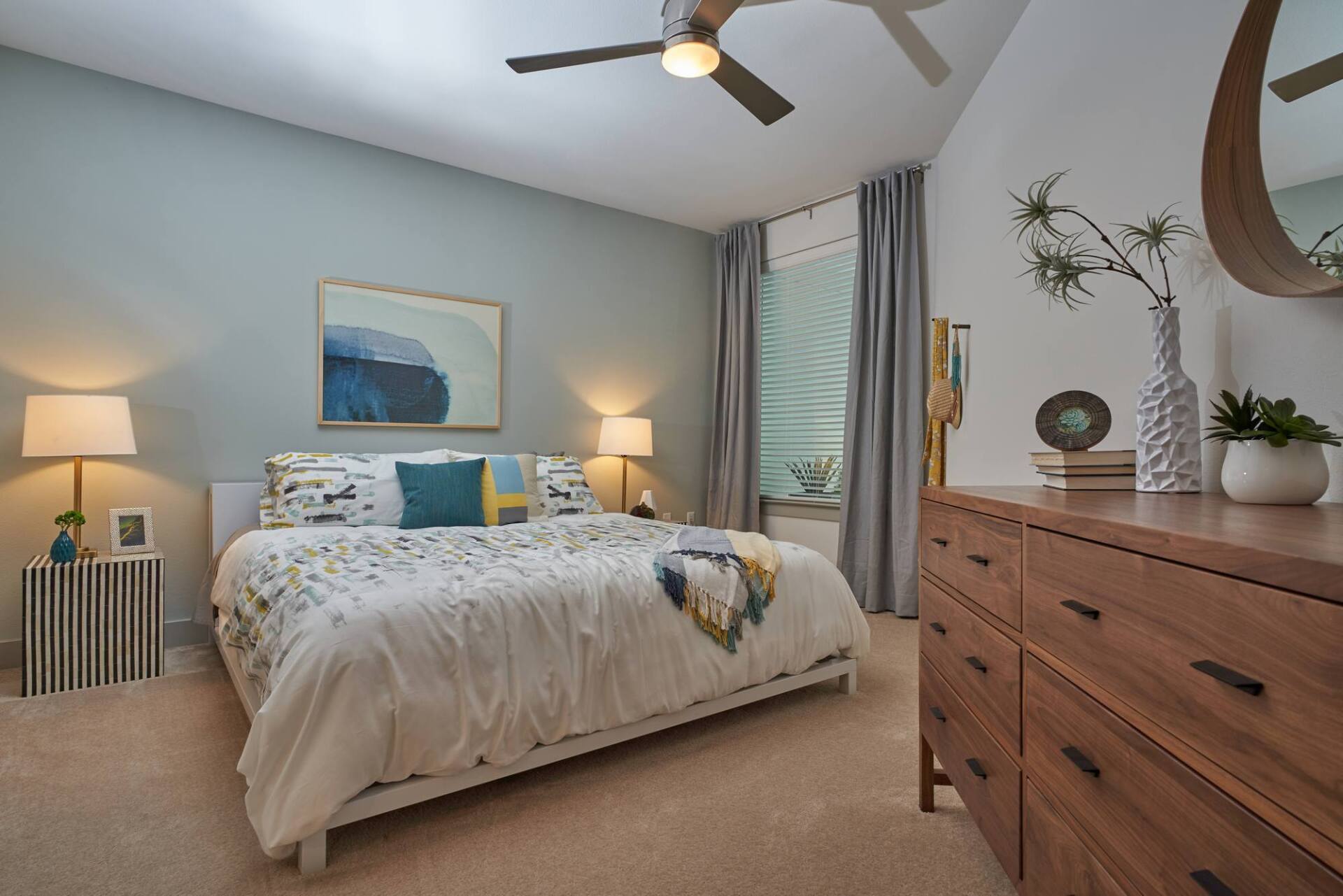 Bedroom with a bed, dresser, lamps, and a window with curtains. Walls are light blue.