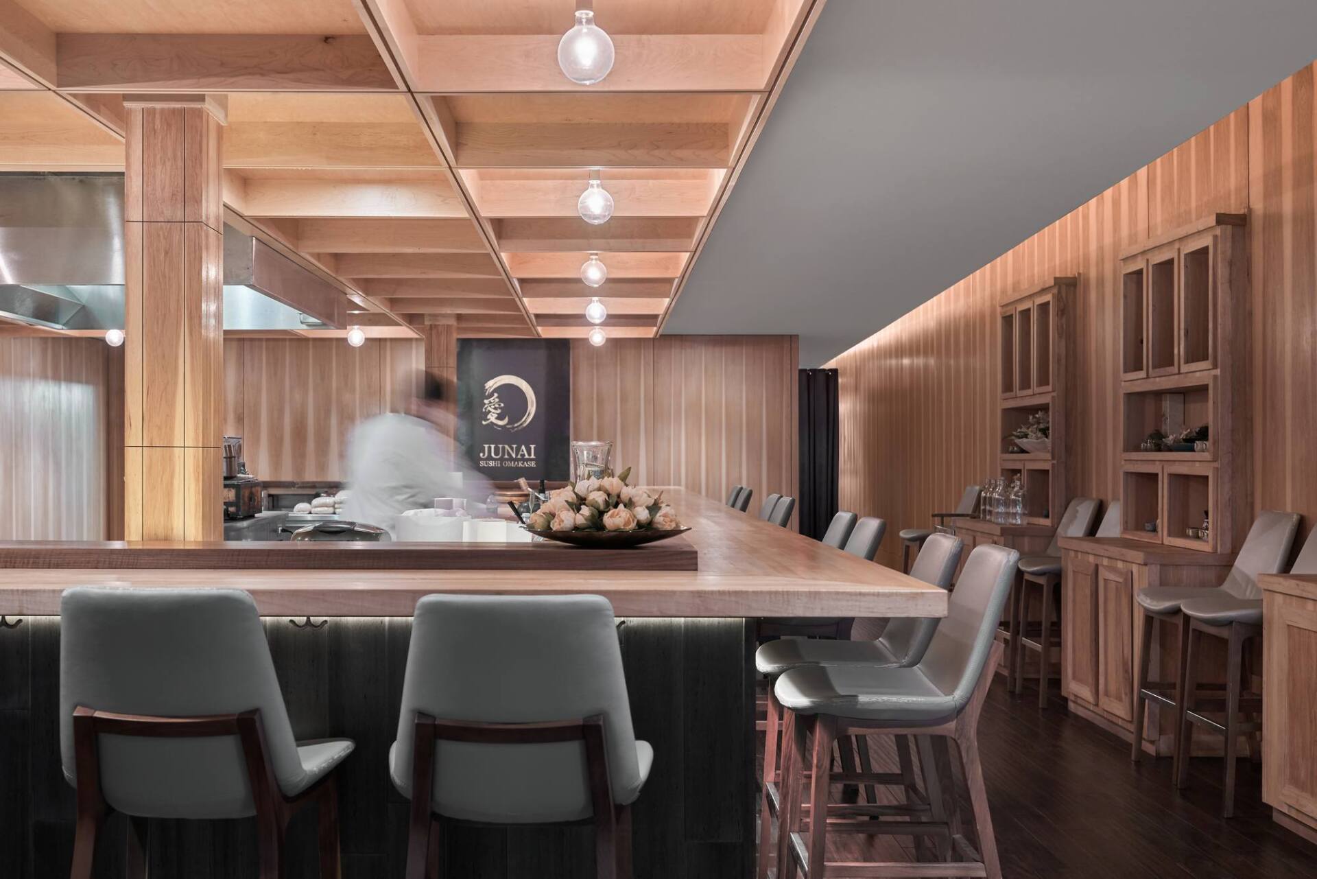 A sushi restaurant interior with a wooden bar, stools, and chef preparing food.