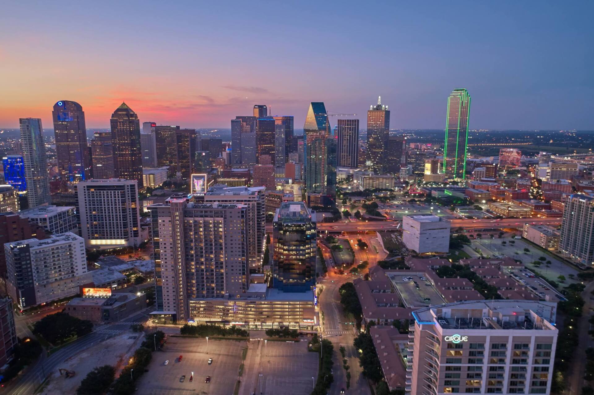 Downtown Dallas skyline at dusk, with illuminated buildings against a twilight sky.