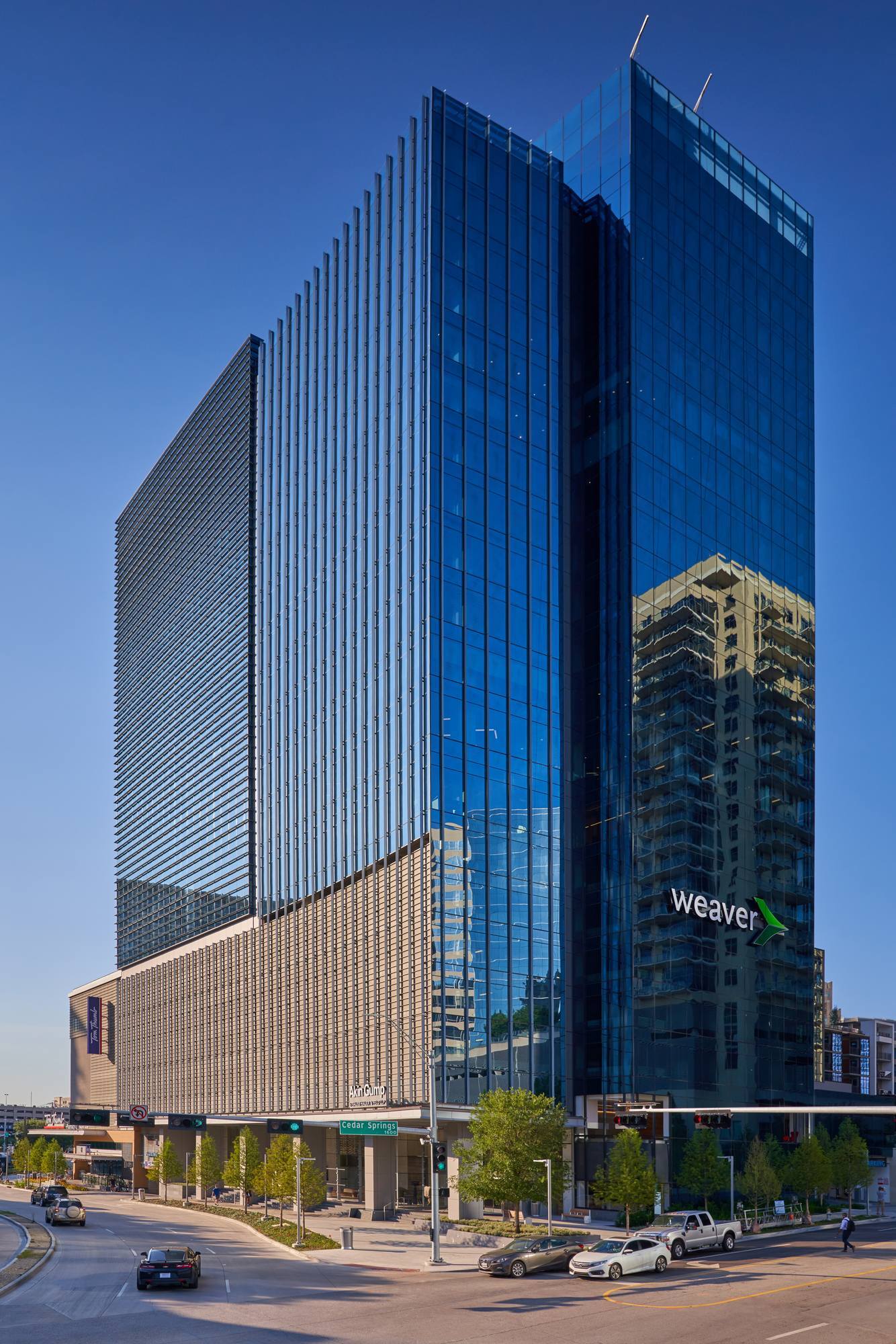 Modern glass skyscraper with a patterned facade, reflecting buildings and blue sky.