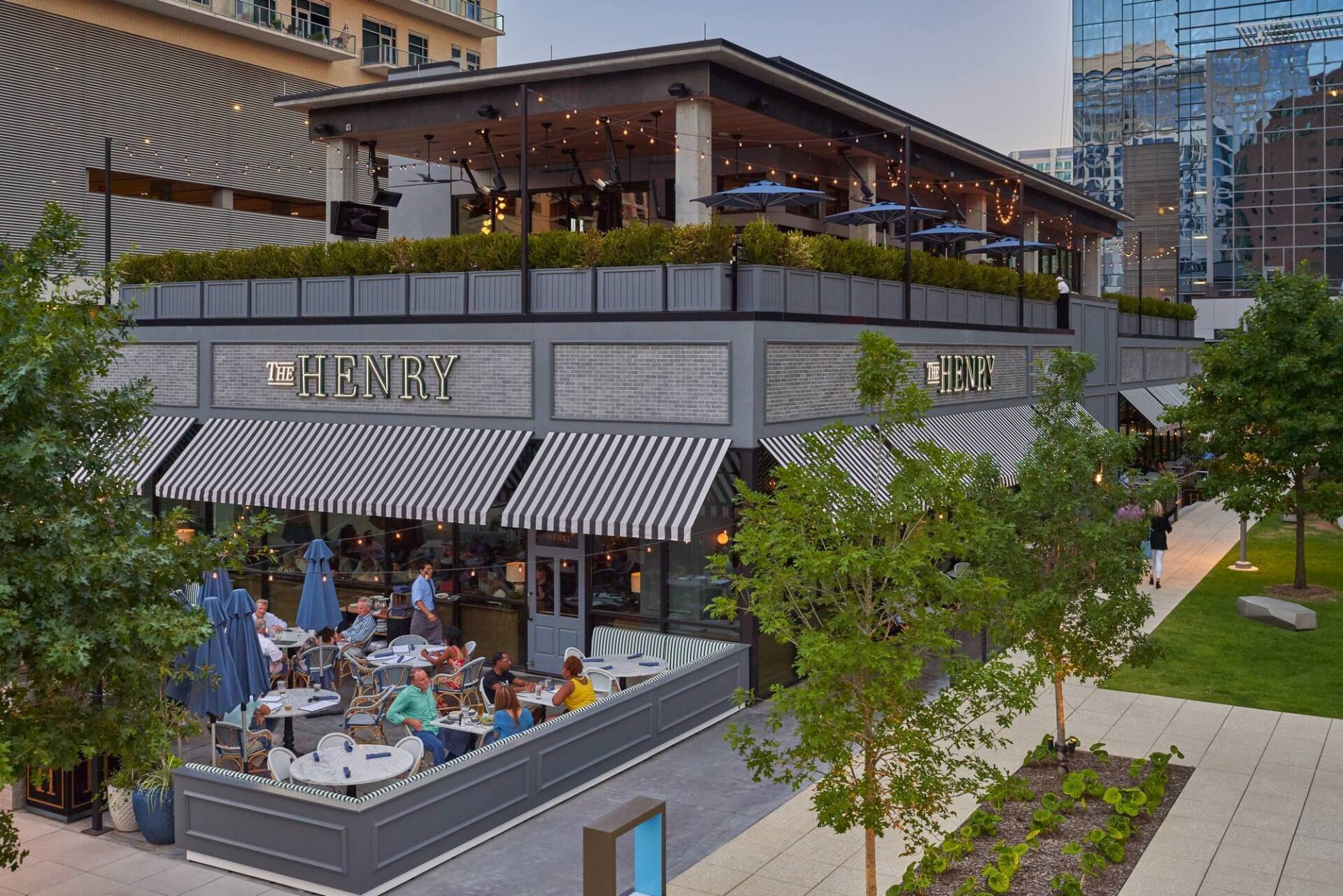 Restaurant with outdoor seating, black and white striped awnings, and a second-floor patio with tables and a modern design.