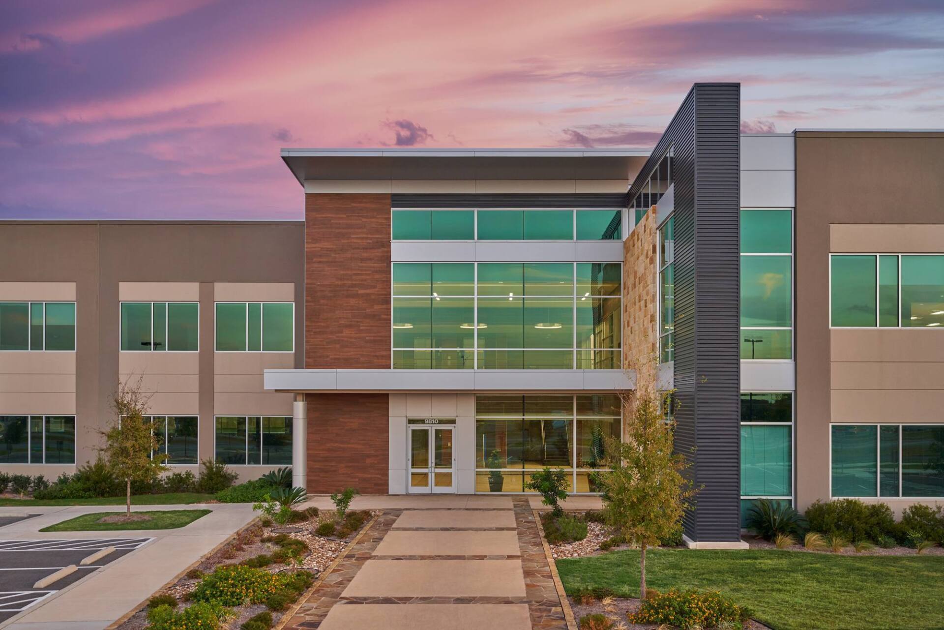 Modern two-story building with glass and brick facade, pathway leading to entrance.