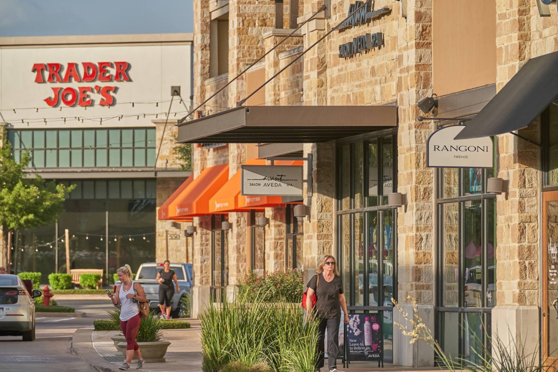 Shops with stone facade, including Trader Joe's, with pedestrians on sidewalk.