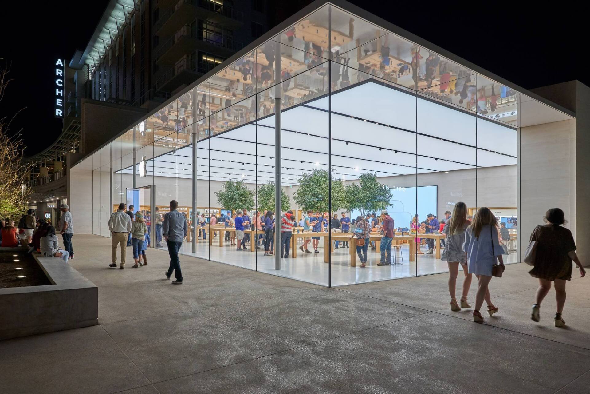 Apple store at night with glass walls and a crowd of people inside and outside.