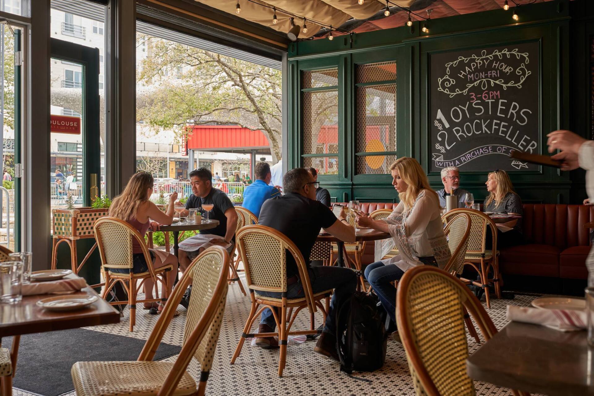 Restaurant interior with patrons seated at tables, a chalkboard menu, and an open view to the street.