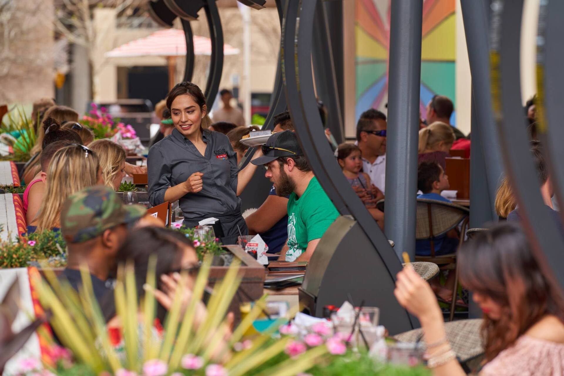 Waitress in gray shirt at outdoor restaurant with patrons.