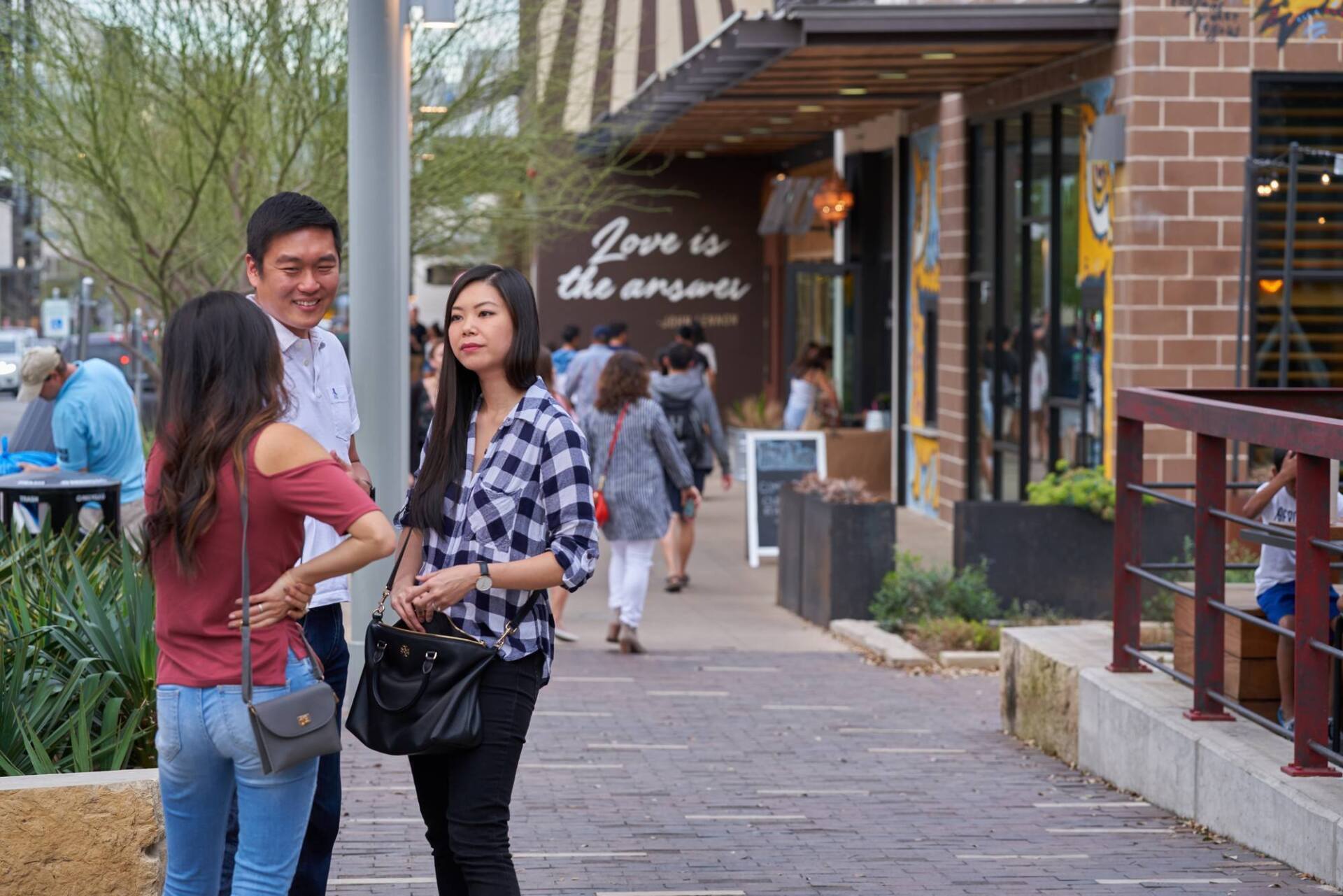 Three people standing and talking on a sidewalk outside a restaurant. 
