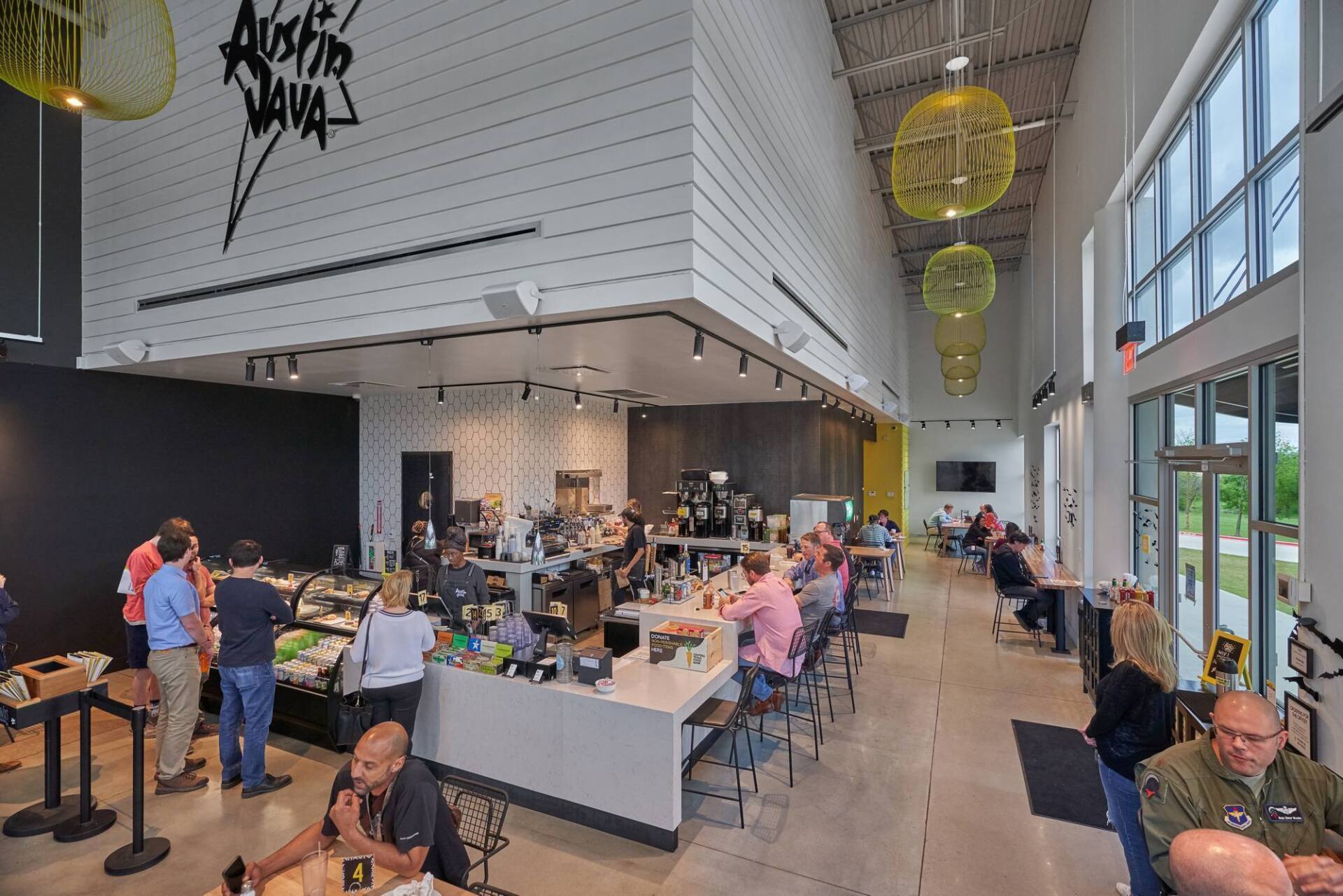 Interior of Austin Java coffee shop with customers, bar, and outdoor view. White, black, and yellow accents.