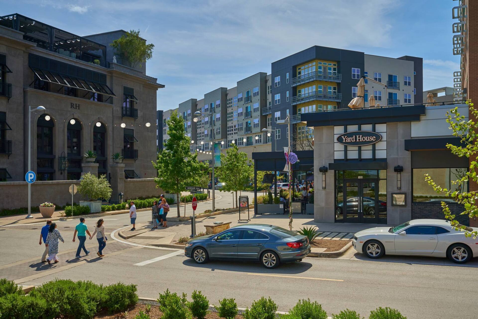 Street scene with buildings, cars, and people walking. Sunny day, modern architecture.