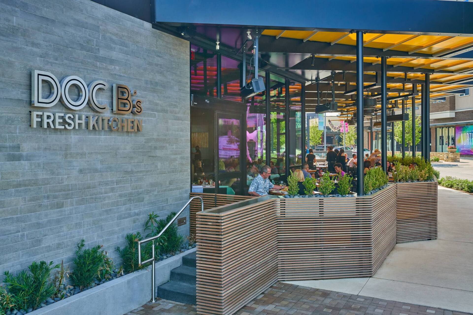 Doc B's Fresh Kitchen restaurant exterior with outdoor seating and gray brick facade.