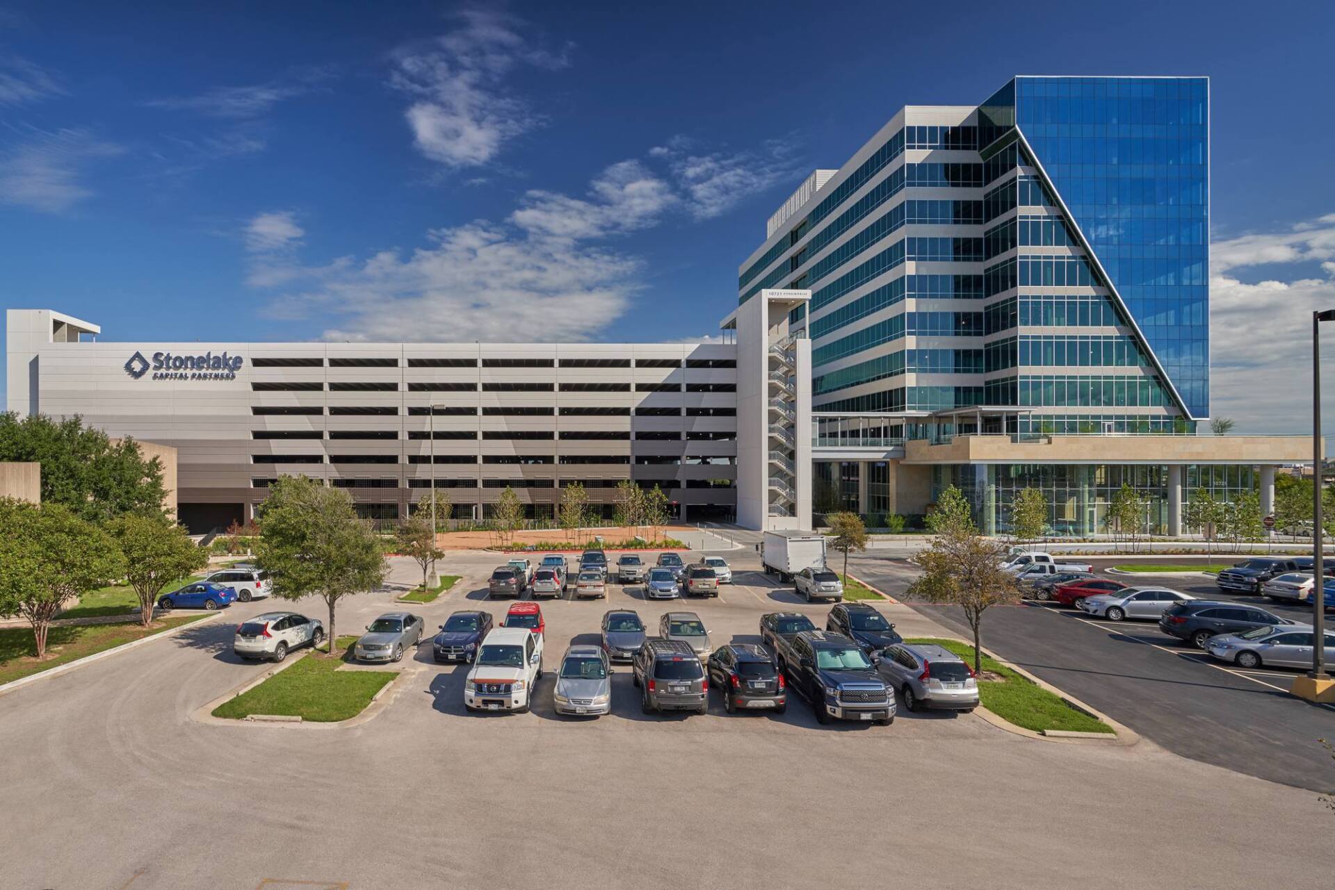 Modern multi-story hospital building with a parking lot under a blue sky.