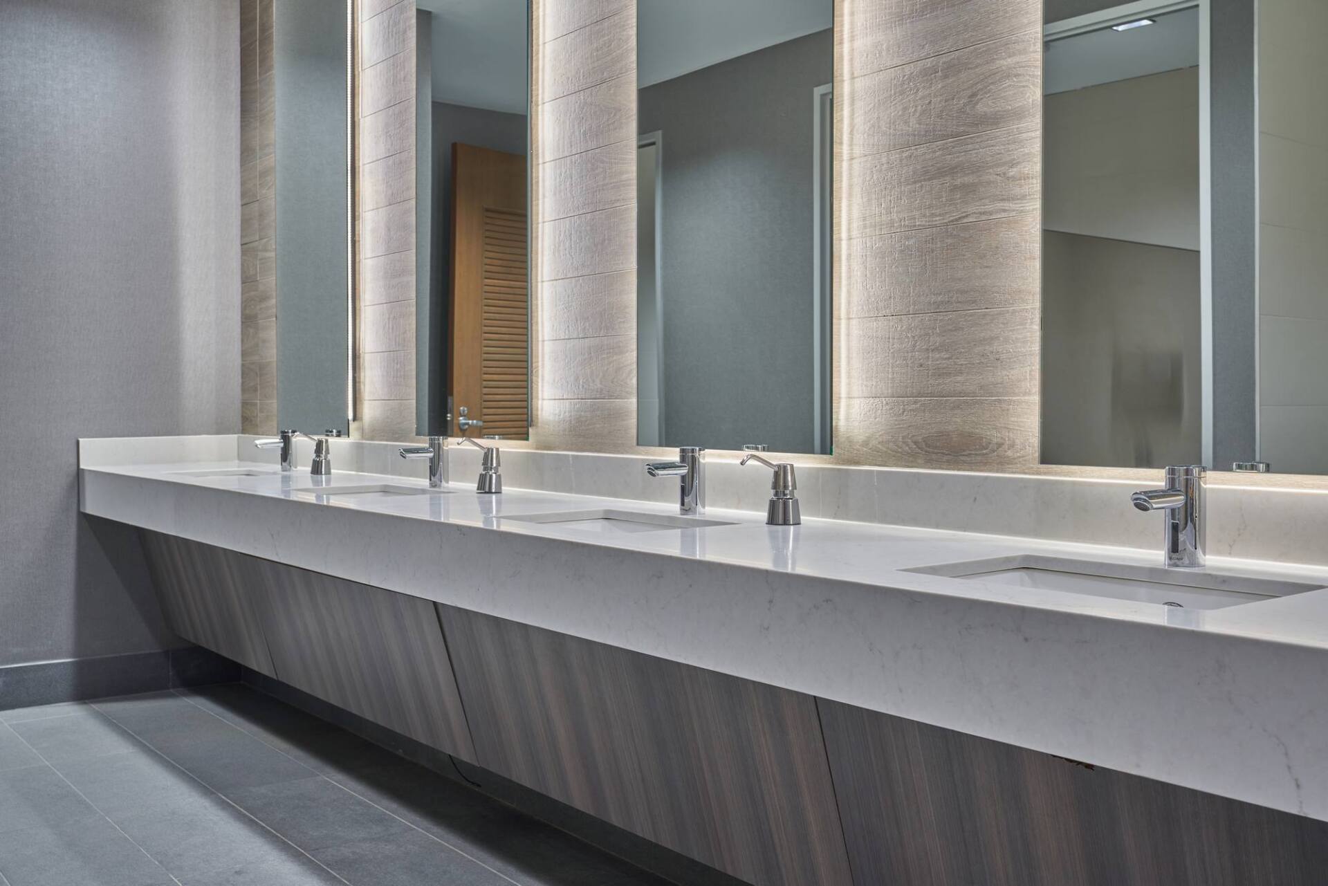 Modern public restroom with long white countertop sinks, mirrors, and columns.