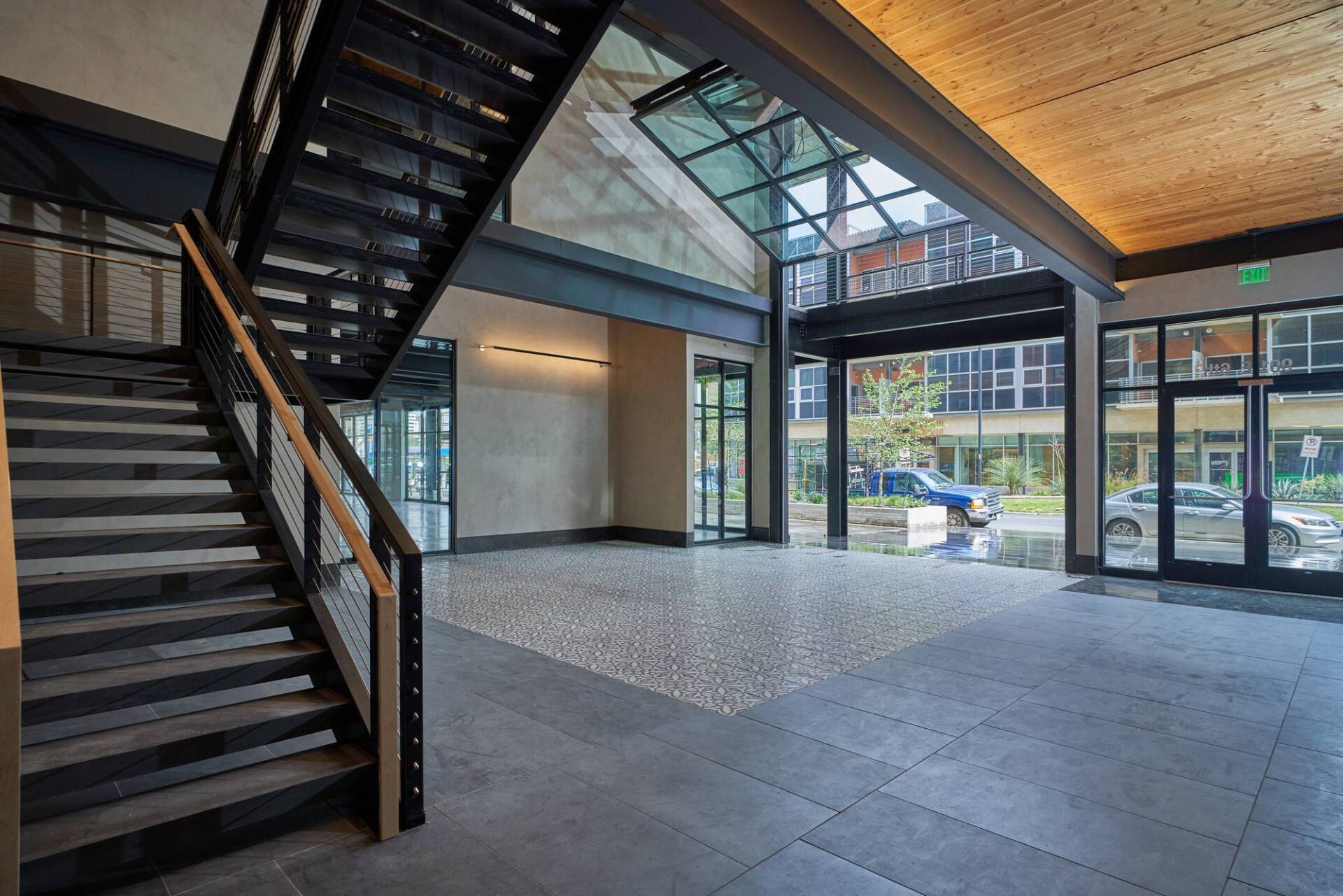 Interior of a modern building with a staircase, concrete floor, and glass garage-style door leading outside.