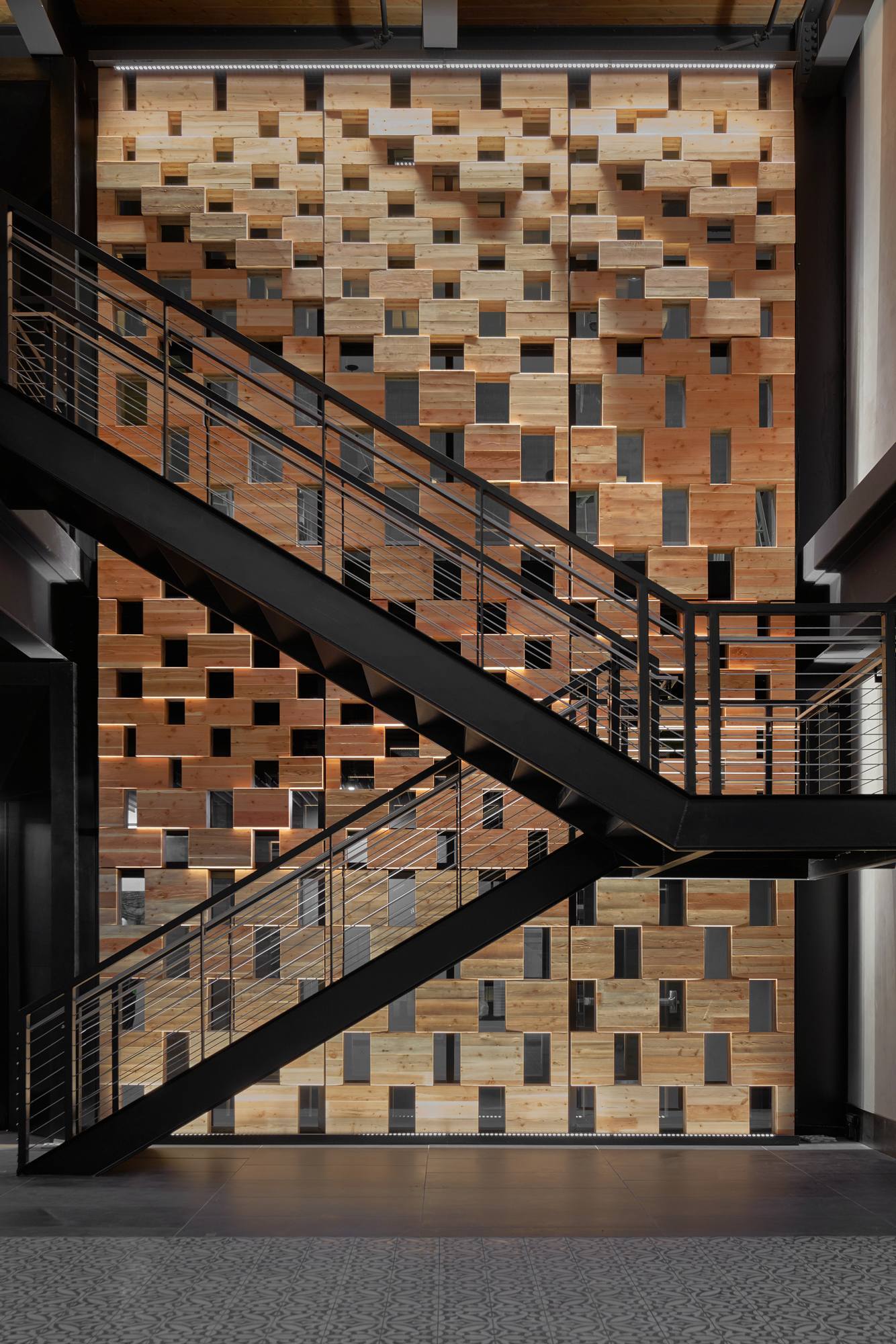 Staircase with black steel supports against a wood panel wall with rectangular cutouts.