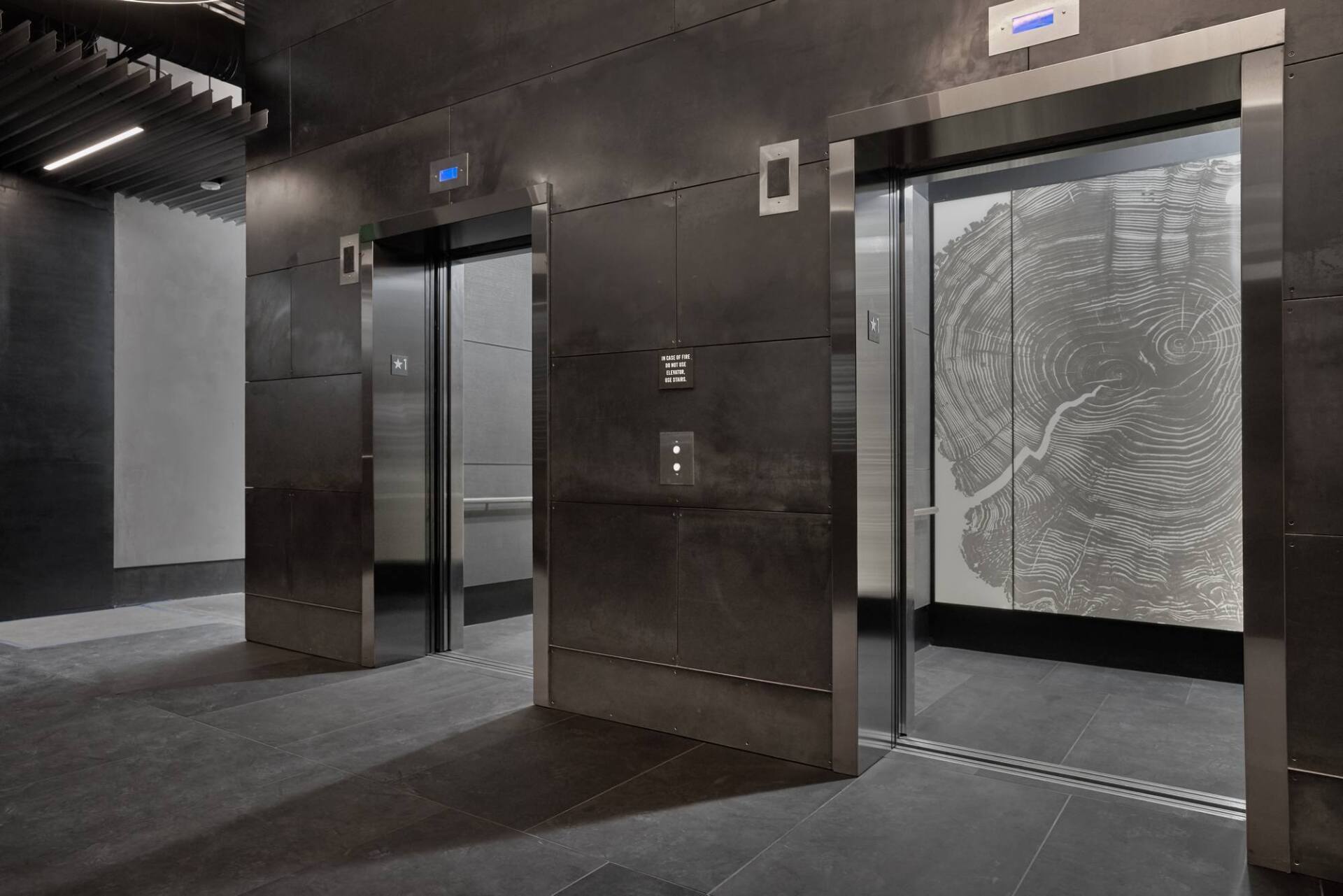 Elevator lobby with three stainless steel elevators, one door open with map design. Dark flooring.