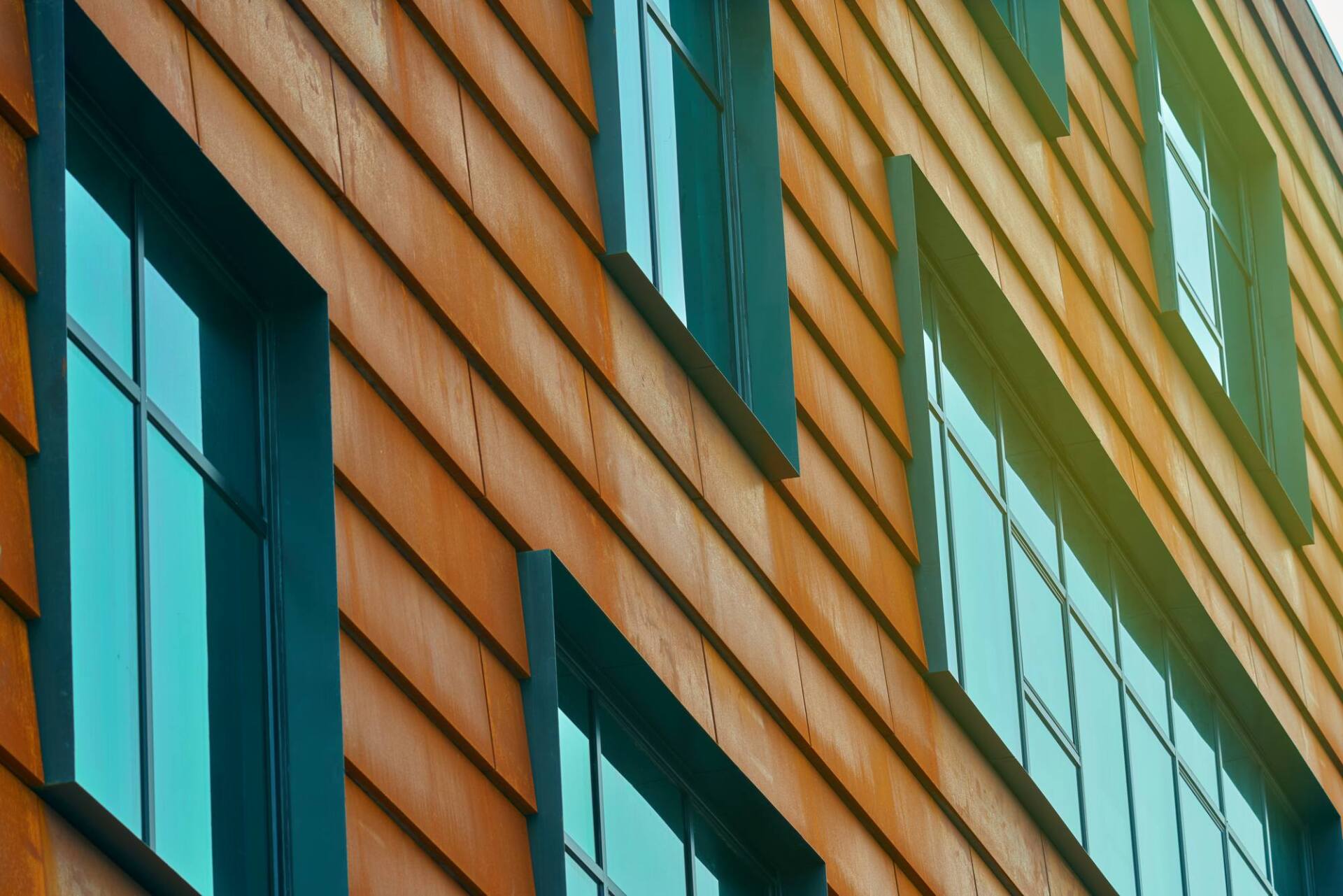Wooden building exterior with teal-framed windows reflecting the sky.