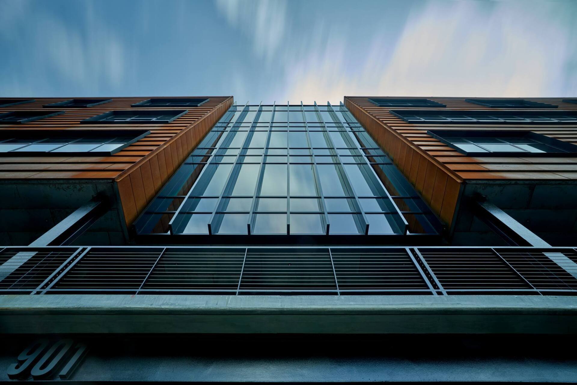 Low-angle view of a modern building with a glass center and brick sides, against a cloudy blue sky.