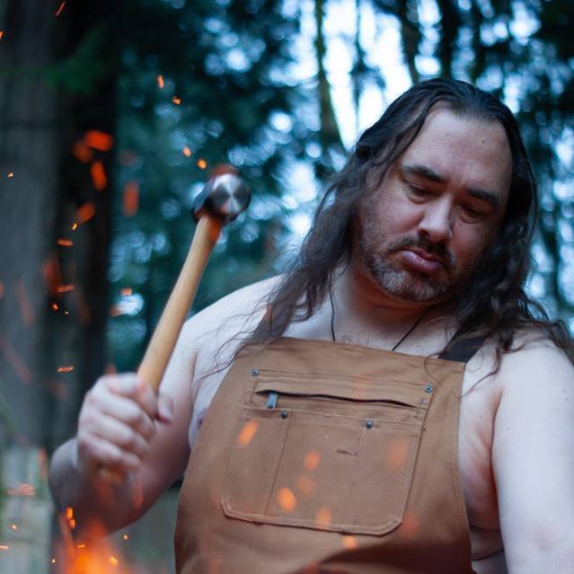 A man in an apron is holding a wooden stick,  representing Hephaestus.