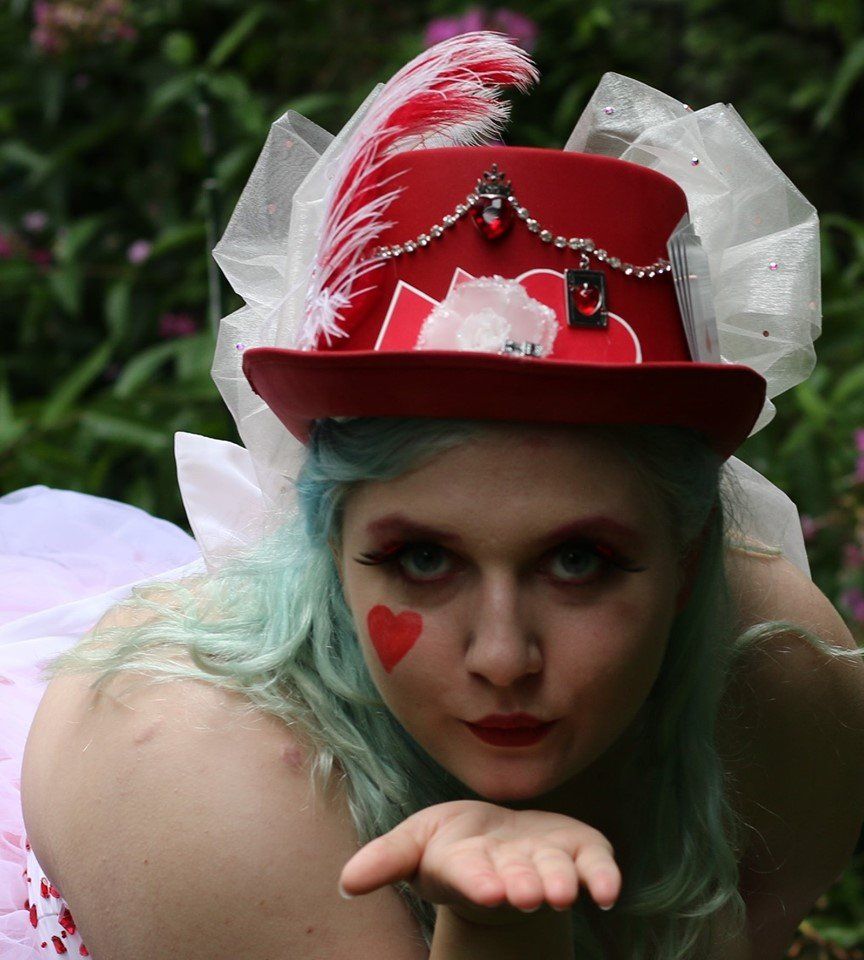 A woman wearing a red top hat with a heart on her face, representing Fortuna.