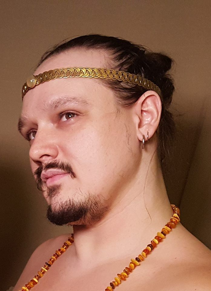 A man with a beard is wearing a headband and a necklace, representing Apollo.