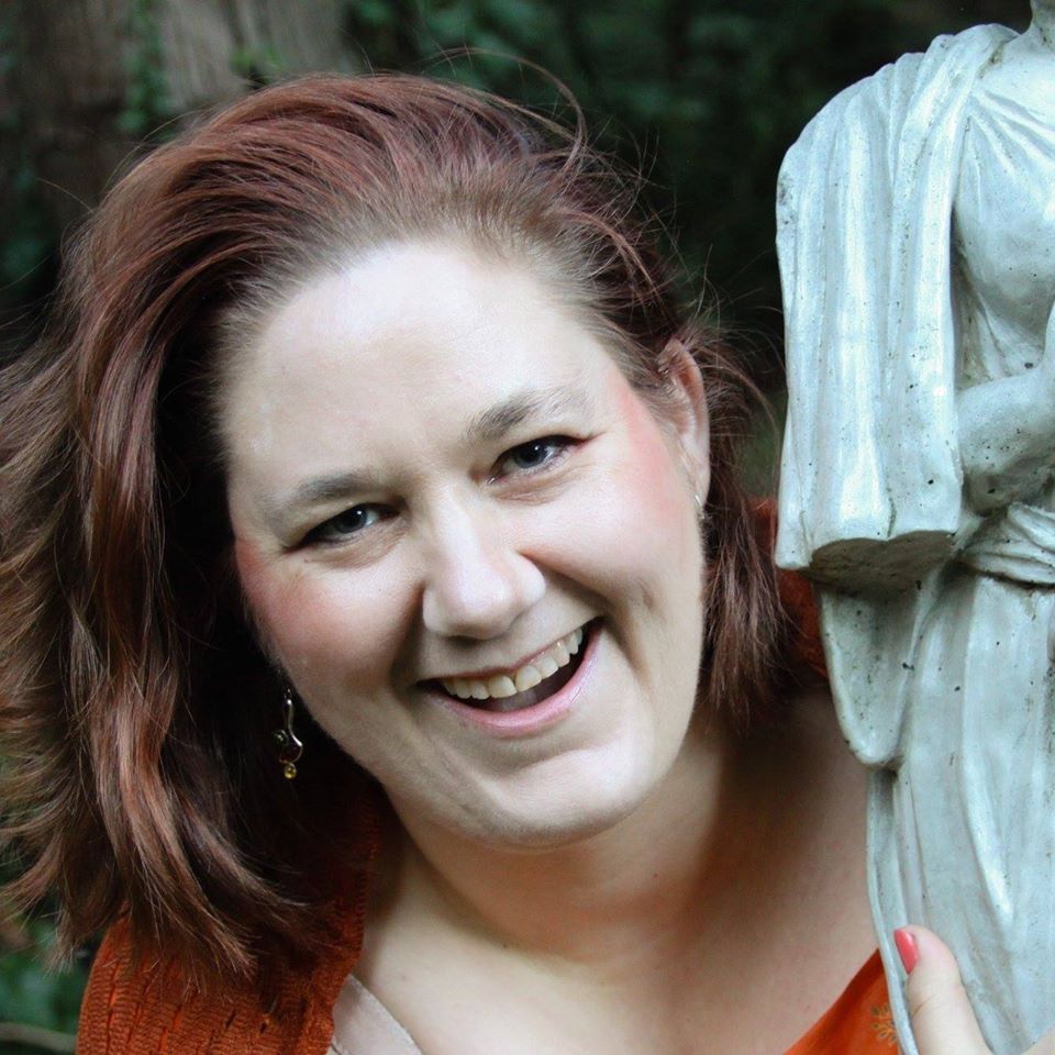 A woman is smiling in front of a statue, representing Baubo.