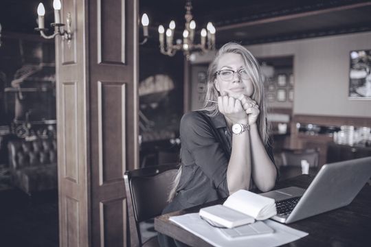 A woman is sitting at a table with a laptop and a book.