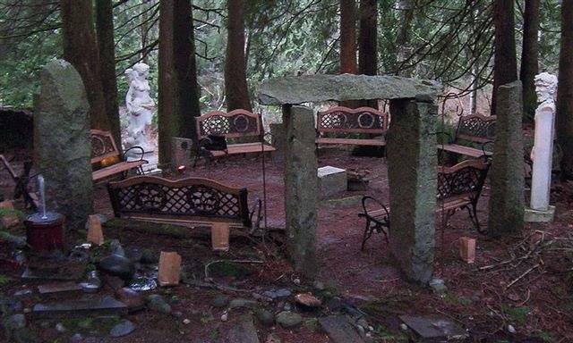 A group of stone benches are sitting in the middle of a forest and henge.