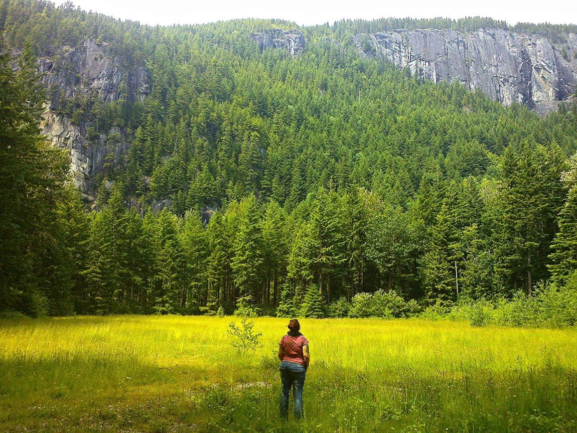 A woman is standing in a field with trees in the background.