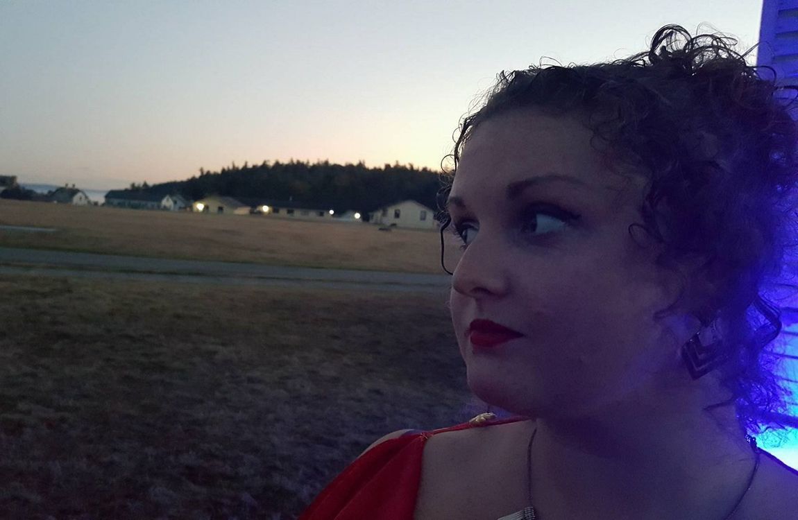 A woman in a red dress is standing in a field at night, a member of the Aquarian Tabernacle Church.