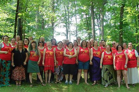 A large group of women are posing for a picture in front of trees,  members of the Aquarian Tabernacle Church.