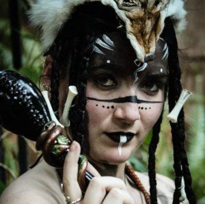A woman is wearing a mask and holding a bottle, representing Hekate.