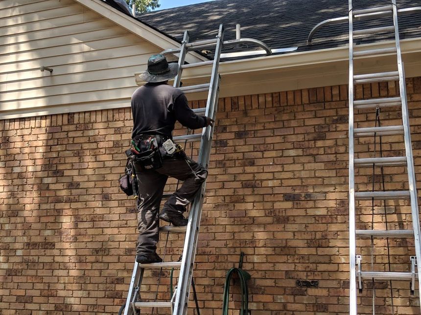 A man is standing on a ladder in front of a brick building.