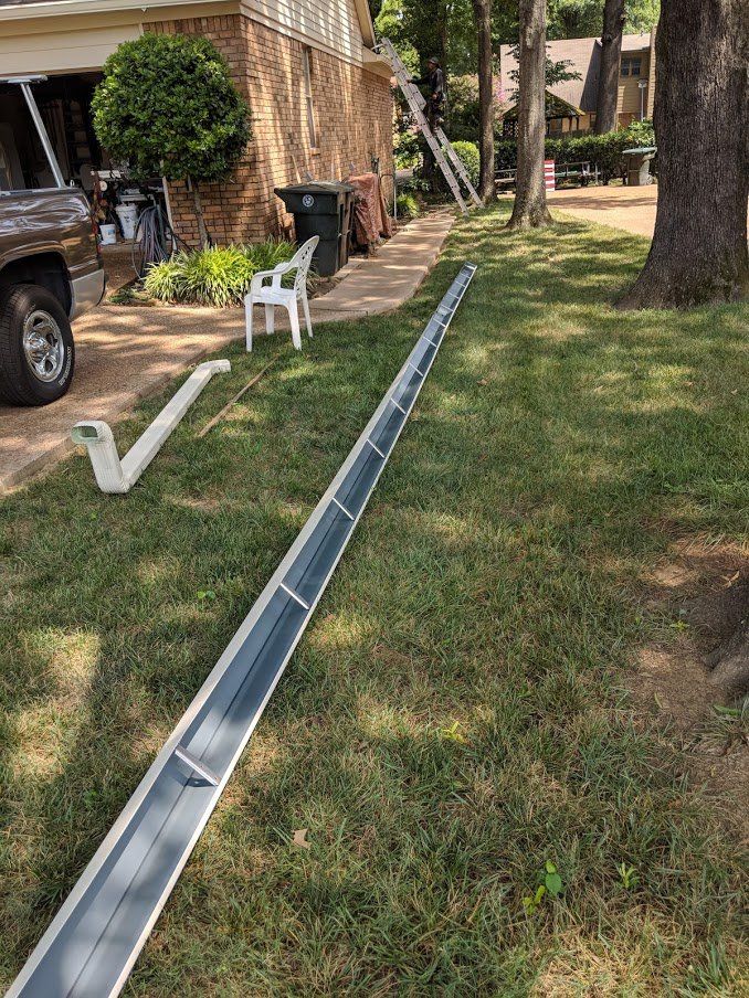 A gutter is sitting in the grass in front of a house.