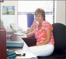 A woman is sitting at a desk talking on a phone