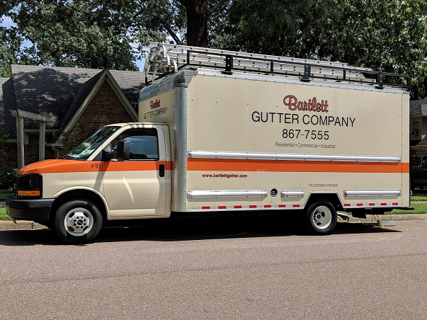 A white and orange gutter company truck is parked on the side of the road.