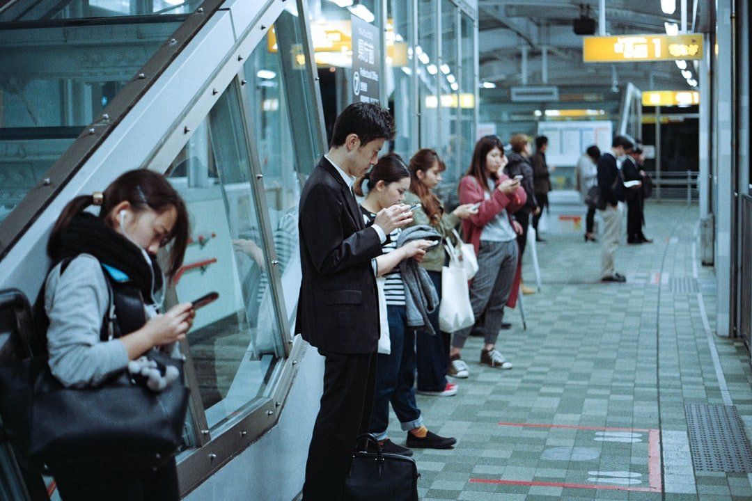 A group of people are standing on a subway platform looking at their phones.