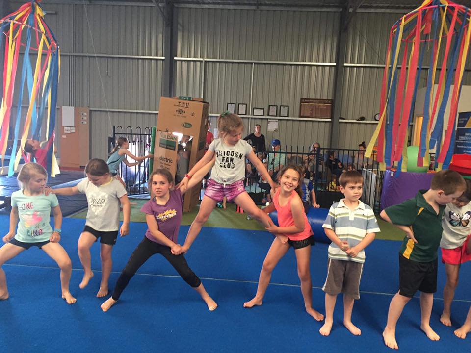 A group of children are standing on a blue mat in a gym.
