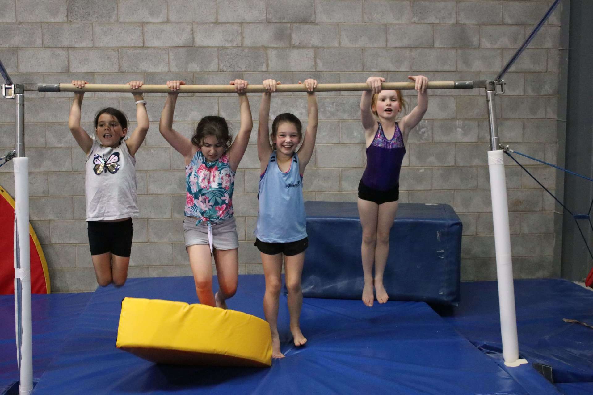 A group of young girls are hanging on a bar in a gym.