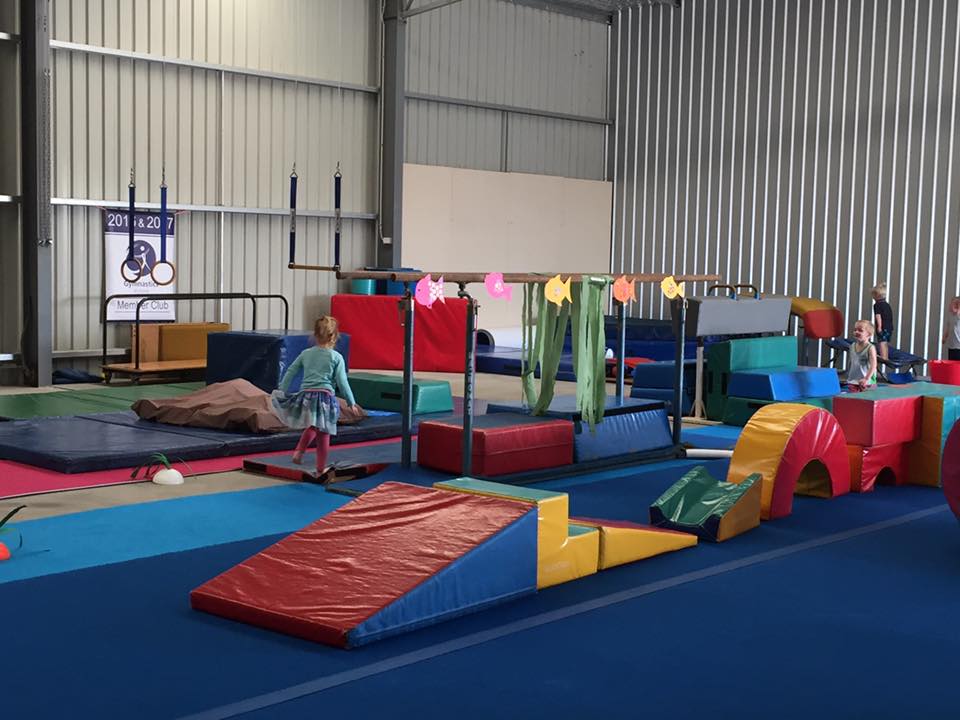 A little girl is standing on a balance beam in a gym.