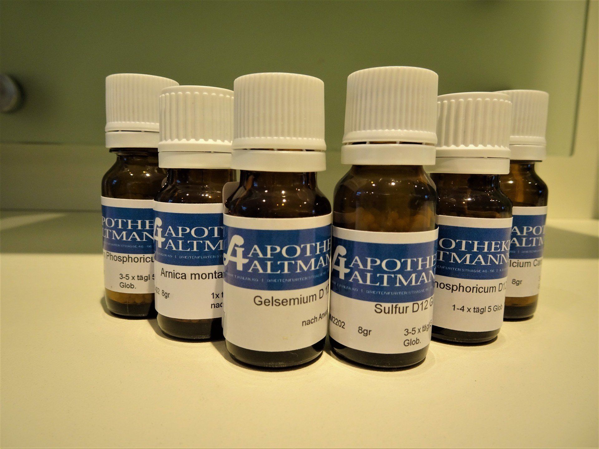 Fünf kleine braune Apothekerfläschchen mit weißen Deckeln und blauen Etiketten standen aufgereiht auf einer Theke.