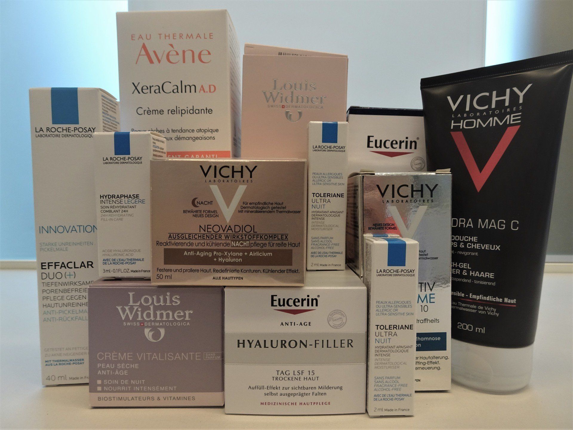 Verschiedene Hautpflegeprodukte in Schachteln und Tuben von Avène, Vichy, Eucerin und L'Occitane auf einem Tisch.